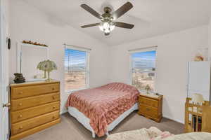 Bedroom featuring multiple windows, vaulted ceiling, light colored carpet, and ceiling fan