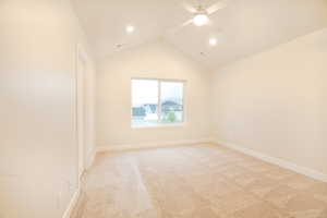 Empty room featuring light colored carpet, ceiling fan, visible vents, and vaulted ceiling