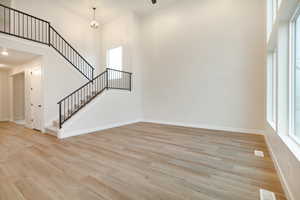 Unfurnished living room with stairs, a high ceiling, baseboards, and light wood finished floors