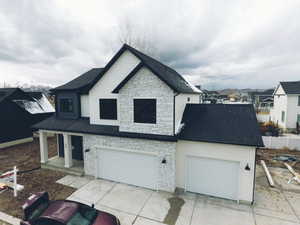 View of front facade featuring a garage, stone siding, driveway, and a shingled roof