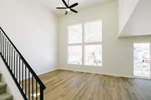 Unfurnished living room featuring baseboards, a ceiling fan, stairs, and wood finished floors