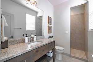 Bathroom with a tile shower, vanity, tile patterned flooring, and toilet