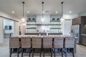 Kitchen featuring stainless steel fridge, a kitchen breakfast bar, decorative backsplash, a barn door, and a center island with sink