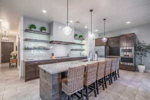 Kitchen with dark brown cabinetry, a breakfast bar, pendant lighting, stainless steel appliances, and a kitchen island with sink