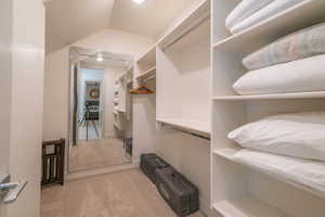 Walk in closet with vaulted ceiling and light carpet