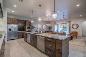 Kitchen with appliances with stainless steel finishes, decorative light fixtures, sink, dark brown cabinets, and a spacious island