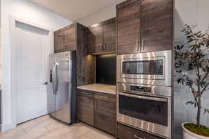 Kitchen featuring appliances with stainless steel finishes, light stone countertops, and dark brown cabinets