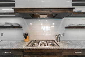 Kitchen with light stone counters, decorative backsplash, stainless steel gas cooktop, and dark brown cabinets