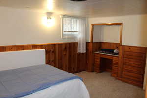 Carpeted bedroom featuring built in desk and wooden walls