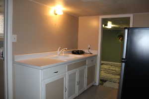 Kitchen featuring stainless steel fridge, sink, and white cabinets