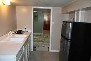 Kitchen featuring white cabinetry, light colored carpet, stainless steel fridge, and sink