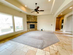 Living room with a stone fireplace, a raised ceiling, and ceiling fan