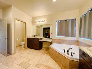 Bathroom featuring vanity, toilet, and tiled bath