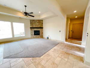 Unfurnished living room with ceiling fan, a fireplace, and a raised ceiling