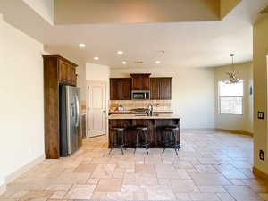 Kitchen with a breakfast bar, an inviting chandelier, appliances with stainless steel finishes, a kitchen island with sink, and backsplash