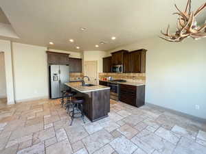 Kitchen featuring dark brown cabinetry, sink, a center island with sink, appliances with stainless steel finishes, and decorative backsplash