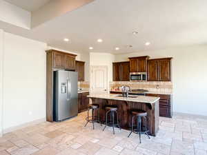 Kitchen with sink, appliances with stainless steel finishes, a center island with sink, tasteful backsplash, and a kitchen bar