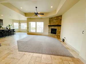 Living room with a raised ceiling, ceiling fan with notable chandelier, and a fireplace