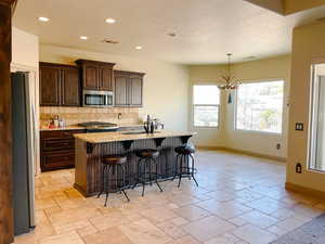 Kitchen with sink, a breakfast bar area, appliances with stainless steel finishes, an island with sink, and decorative backsplash