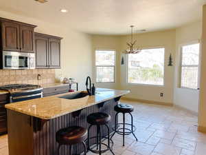 Kitchen featuring sink, decorative backsplash, dark brown cabinetry, stainless steel appliances, and a center island with sink