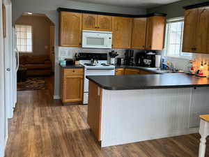 Kitchen with tasteful backsplash, dark hardwood / wood-style flooring, white appliances, and kitchen peninsula