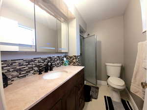 Bathroom featuring tasteful backsplash, vanity, toilet, and an enclosed shower