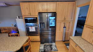 Kitchen featuring light brown cabinetry, light stone countertops, light hardwood / wood-style floors, and appliances with stainless steel finishes