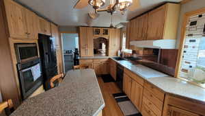 Kitchen featuring sink, a textured ceiling, pendant lighting, light hardwood / wood-style floors, and black appliances