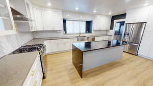 Kitchen with a kitchen island, white cabinetry, sink, stainless steel appliances, and light wood-type flooring