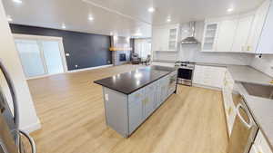 Kitchen featuring a center island, light hardwood / wood-style flooring, white cabinets, stainless steel appliances, and wall chimney range hood