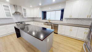 Kitchen with white cabinets, stainless steel appliances, light hardwood / wood-style floors, and wall chimney exhaust hood