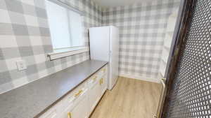 Kitchen with white cabinetry, white refrigerator, and light hardwood / wood-style flooring