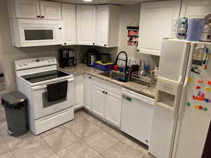 Kitchen with sink, white cabinets, light tile patterned floors, light stone counters, and white appliances