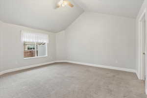 Empty room featuring ceiling fan, lofted ceiling, and light carpet