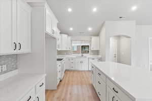 Kitchen featuring sink, light stone countertops, white cabinets, and light wood-type flooring