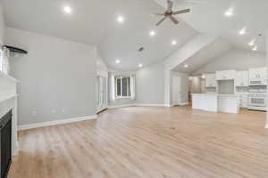 Unfurnished living room featuring ceiling fan, high vaulted ceiling, and light hardwood / wood-style flooring