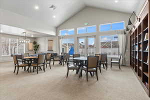 Dining area featuring french doors, light colored carpet, a chandelier, and high vaulted ceiling