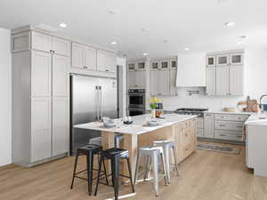 Kitchen featuring premium range hood, a breakfast bar area, a kitchen island, stainless steel appliances, and white cabinets