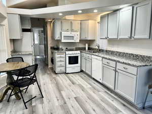 Kitchen featuring sink, gray cabinetry, stone countertops, light wood-type flooring, and white appliances