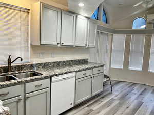 Kitchen with high vaulted ceiling, sink, light stone counters, white dishwasher, and light wood-type flooring