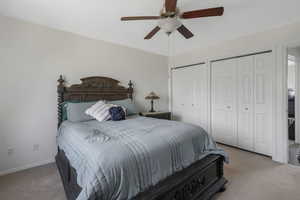 Carpeted bedroom featuring multiple closets and ceiling fan