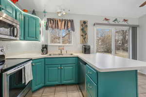 Kitchen with green cabinetry, appliances with stainless steel finishes, kitchen peninsula, and sink