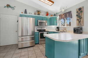 Kitchen featuring lofted ceiling, sink, appliances with stainless steel finishes, light tile patterned flooring, and kitchen peninsula