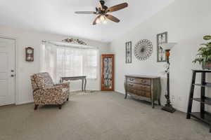 Living area with ceiling fan, vaulted ceiling, and light carpet