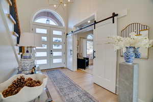 Entrance foyer featuring a high ceiling, a barn door, a chandelier, and light hardwood / wood-style floors