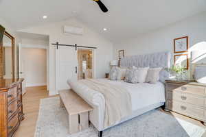 Bedroom with an AC wall unit, lofted ceiling, ceiling fan, a barn door, and light hardwood / wood-style flooring