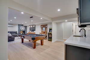 Playroom featuring an AC wall unit, a fireplace, billiards, sink, and light hardwood / wood-style floors