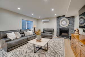 Living room with a tiled fireplace, a wall unit AC, and light hardwood / wood-style floors