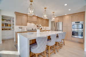 Kitchen with pendant lighting, appliances with stainless steel finishes, light brown cabinetry, and a center island with sink