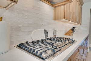 Interior details featuring stainless steel gas stovetop, light brown cabinetry, and backsplash